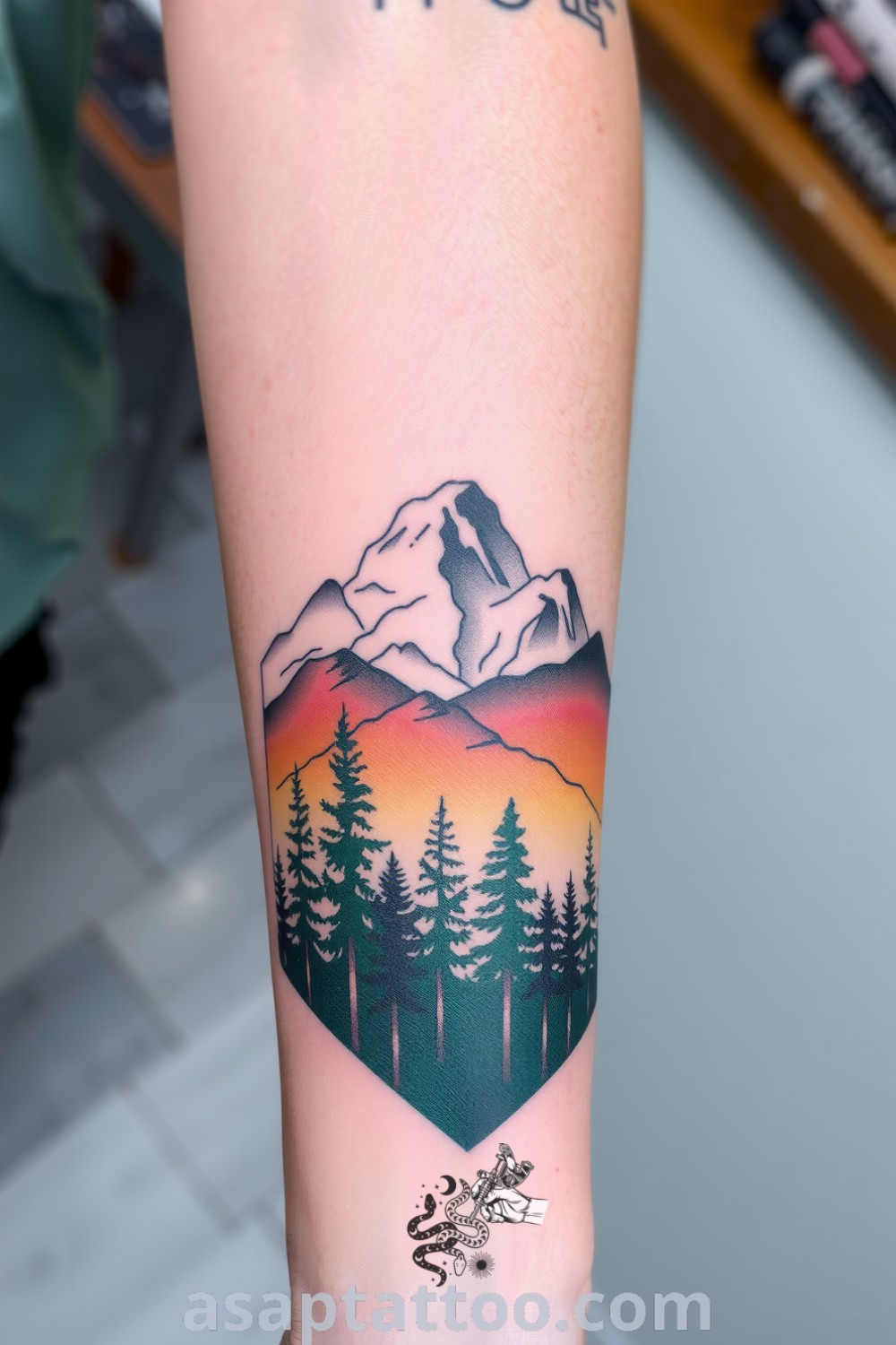 A detailed forest and mountain tattoo on the forearm featuring intricate linework of pine trees and peaks, showcasing deep greens and browns. A gorgeous tattoo idea to inspire you to get inked. asaptattoo.com