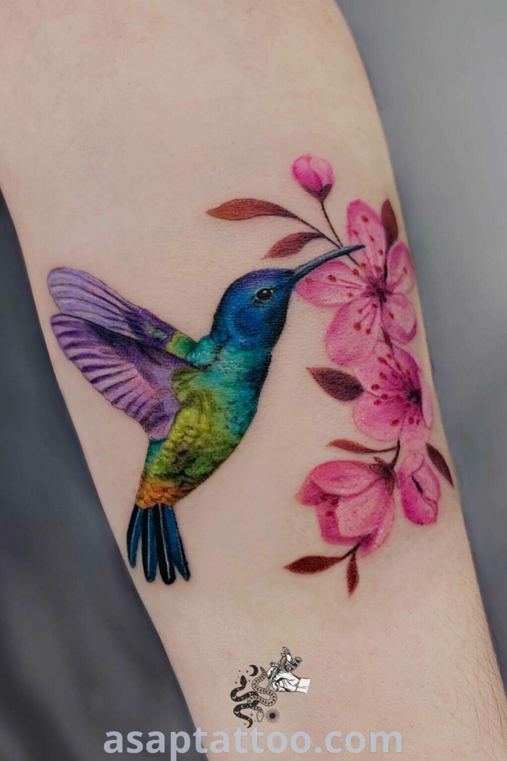 Colorful hummingbird tattoo featuring pink flowers, a stunning design idea for bird tattoos that symbolize beauty and joy. Perfect for women looking for small, elegant tattoos with meaning. Discover more amazing tattoo inspiration at asaptattoo.com.