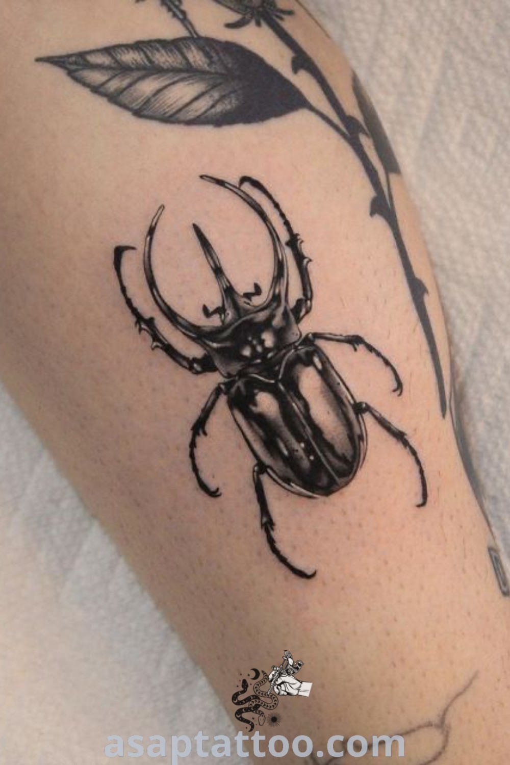 Black and white photo of a rhinosaurus beetle tattoo on the left arm with a flower in the center, showcasing its intricate details. Explore unique insect tattoo designs and find inspiration at asaptattoo.com.