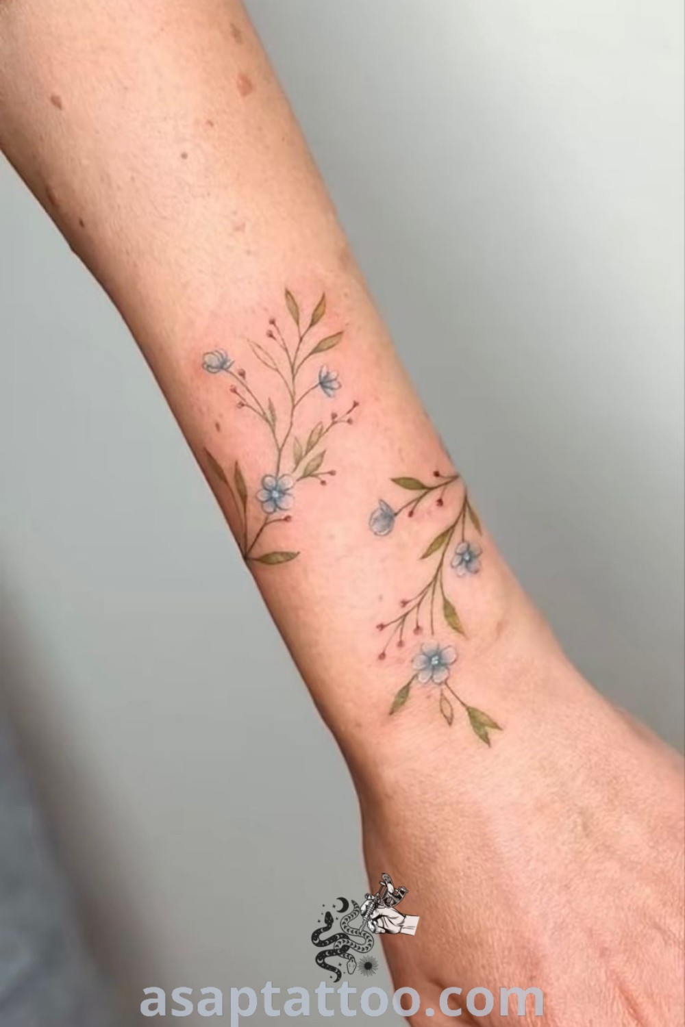 Delicate floral wrist tattoo showcasing colored flowers and leaves on the arm, embodying elegance and artistic beauty. Discover more inspiring tattoo ideas at asaptattoo.com.