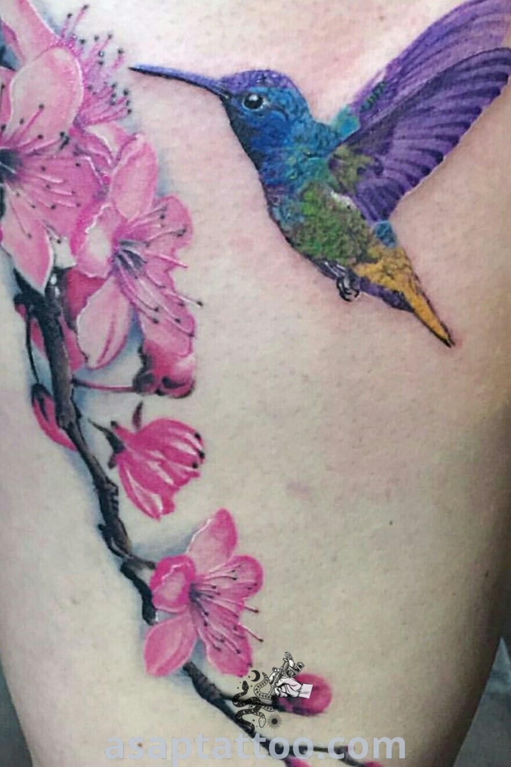 Elegant watercolor tattoo of a hummingbird and pink flowers, showcasing gorgeous artistic features. An inspiring design filled with meaning, perfect for those seeking the best tattoo ideas to decorate their bodies. Explore more at asaptattoo.com.