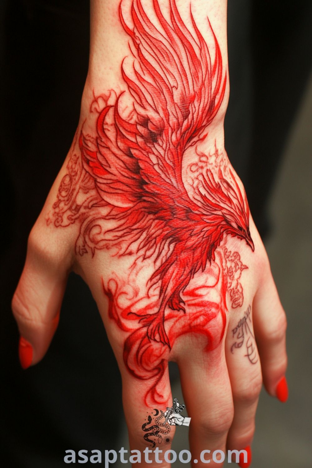 Crimson ink phoenix tattoo on a light-skinned hand featuring dynamic wings and a regal tail, showcasing bold colors and intricate details. An amazing tattoo design that symbolizes rebirth you must see to believe. asaptattoo.com