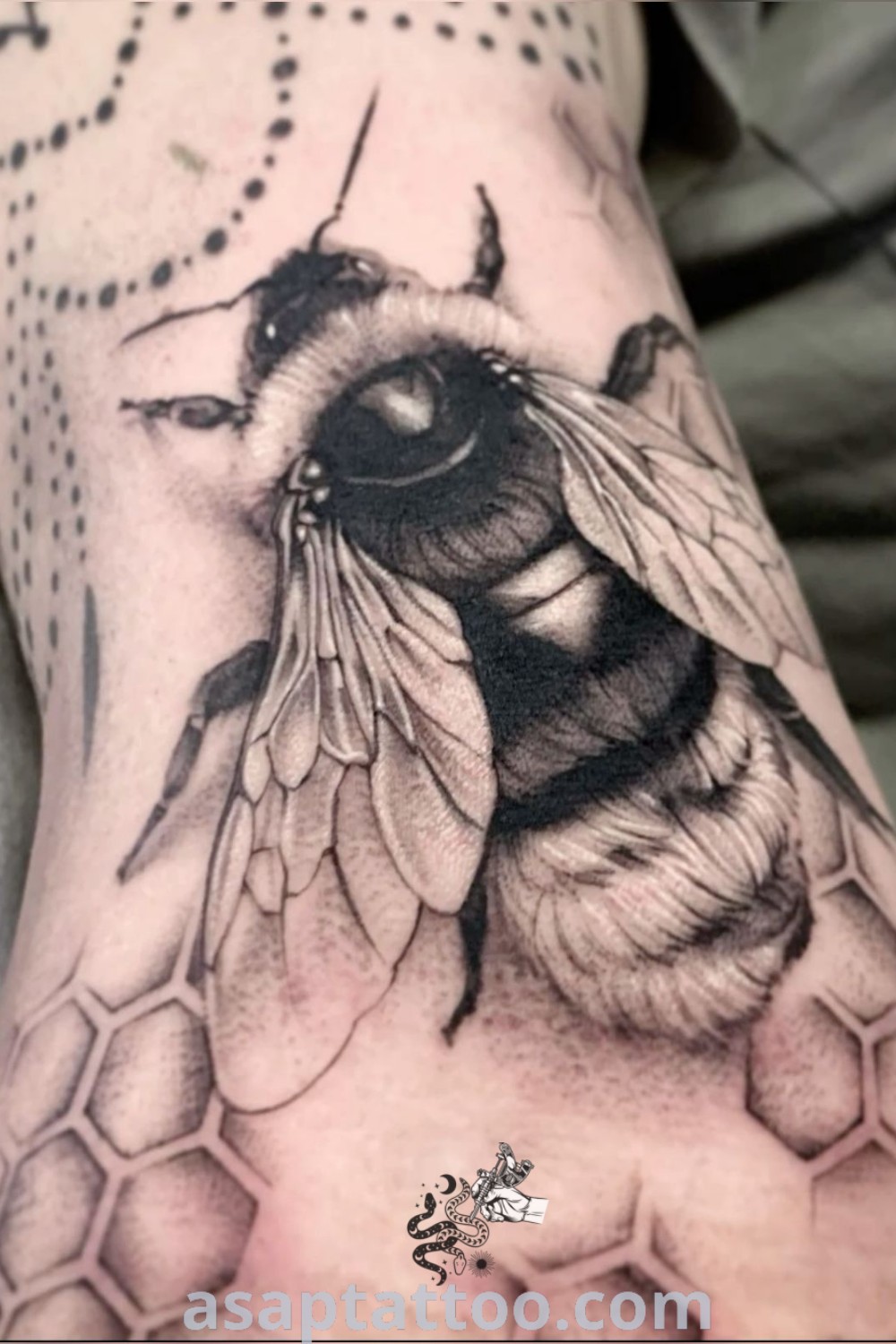 Black and white tattoo of a bee on the arm, featuring intricate honeycomb designs. This beautiful tattoo showcases artistic features that inspire ink lovers. Find the best ideas at asaptattoo.com.