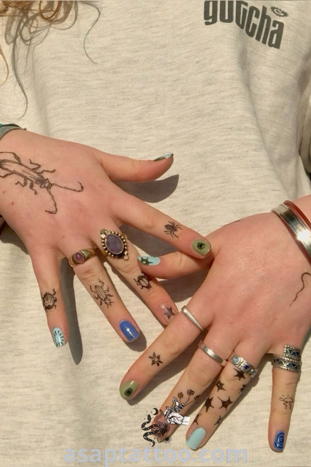 Two women with hand tattoos, including hippy designs and cute knuckle tattoos, holding hands. An inspiring display of artistic body art featuring insect finger tattoos and rings. Explore these amazing ideas at asaptattoo.com.