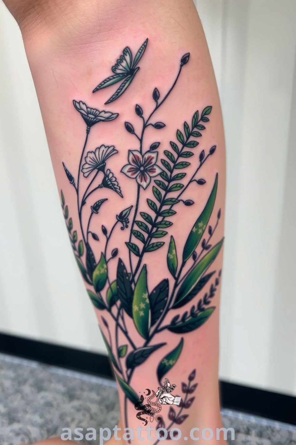 An elegant tattoo design showcasing lush ferns and delicate wildflowers in rich green and soft earth tones. A gorgeous tattoo idea you must see to believe. asaptattoo.com