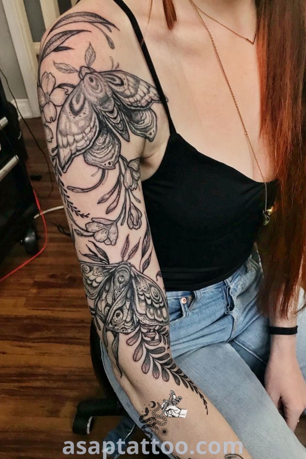 Floral tattoo sleeve on a woman with long red hair sitting on the floor, featuring intricate designs including geometric shapes and moths. Discover amazing tattoo ideas that inspire body art at asaptattoo.com.