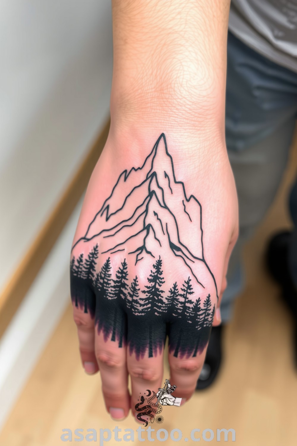 Linework tattoo of mountains and dense forests wrapping around the hand, showcasing intricate details and shading gradients in black ink. An elegant tattoo idea you must see to believe that captures the spirit of adventure. asaptattoo.com