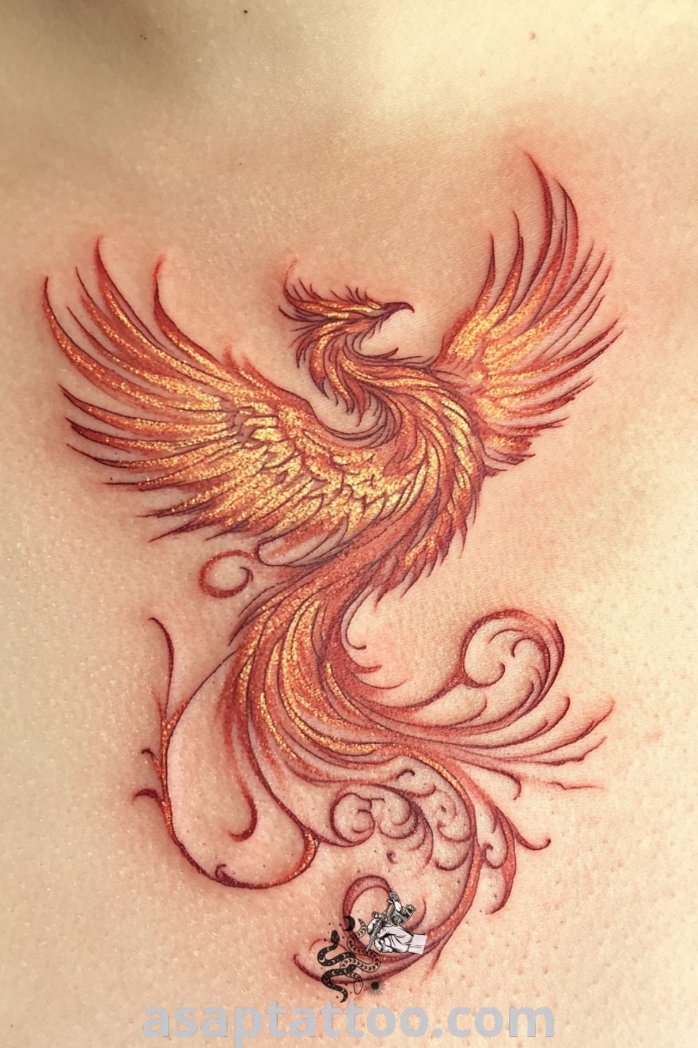 Intricate feminine phoenix tattoo on collarbone in vibrant reds, oranges, and golds, featuring detailed feathers and graceful design elements that symbolize rebirth. A gorgeous tattoo idea you must see to believe. asaptattoo.com