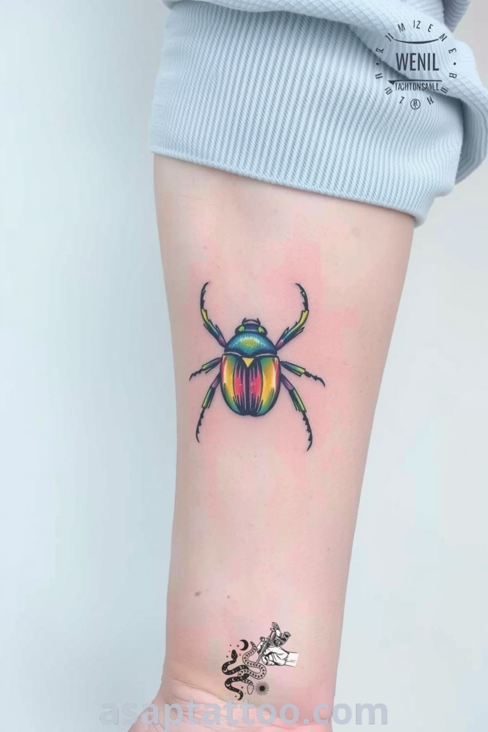 Pastel beetle tattoo on inner arm featuring soft blue, pink, and yellow hues in intricate detail. A gorgeous tattoo that will inspire you to get inked. asaptattoo.com