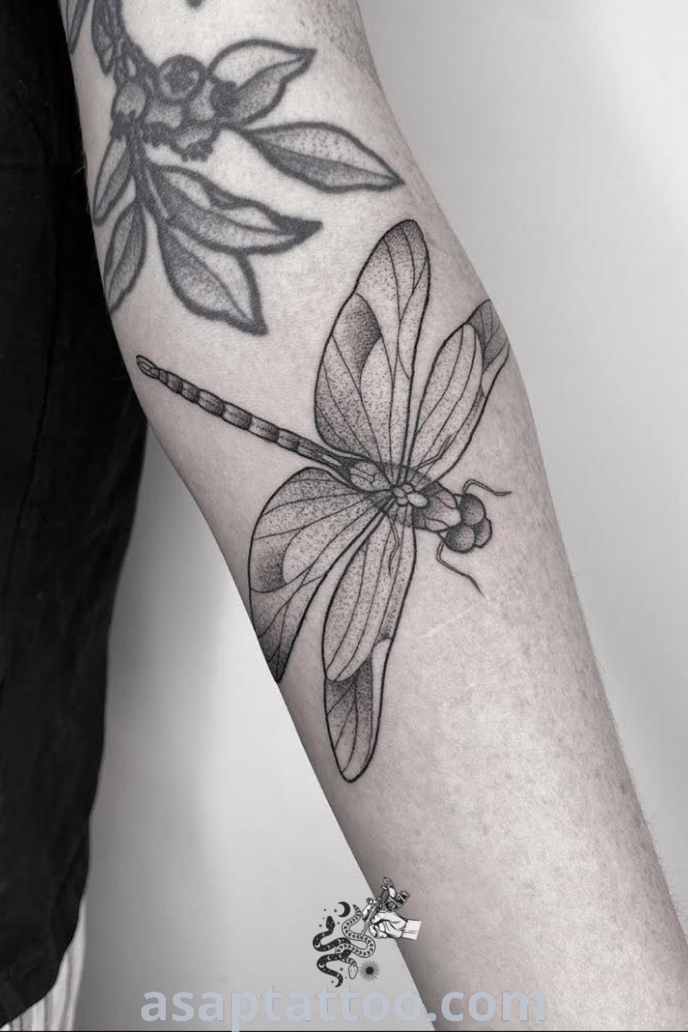 Black and white dragonfly tattoo on the right arm with an arrow, showcasing elegant design elements. A stunning choice for nature lovers and those seeking inspiring tattoo ideas. Discover more at asaptattoo.com.