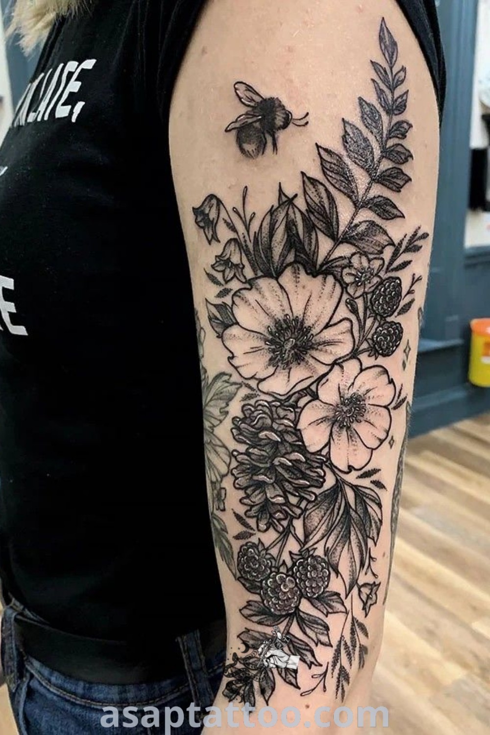A woman showcasing an amazing black and white flower tattoo on her arm, featuring a fern floral tattoo design among other wildflower sleeve tattoos. Discover inspiring tattoo ideas at asaptattoo.com.
