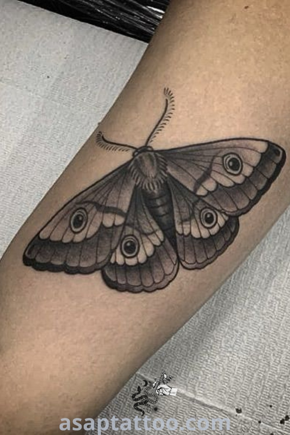 Black and white moth tattoo on the left leg featuring an eyeball, showcasing an elegant design that inspires tattoo lovers looking for amazing cover-up ideas. Discover more at asaptattoo.com.