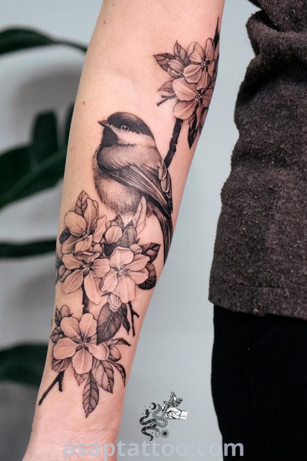 A charming bird in tree tattoo featuring a small bird sitting on a branch surrounded by flowers. An elegant design for women, perfect for arm or forearm tattoos, showcasing artistic features. Explore more amazing tattoo ideas at asaptattoo.com.