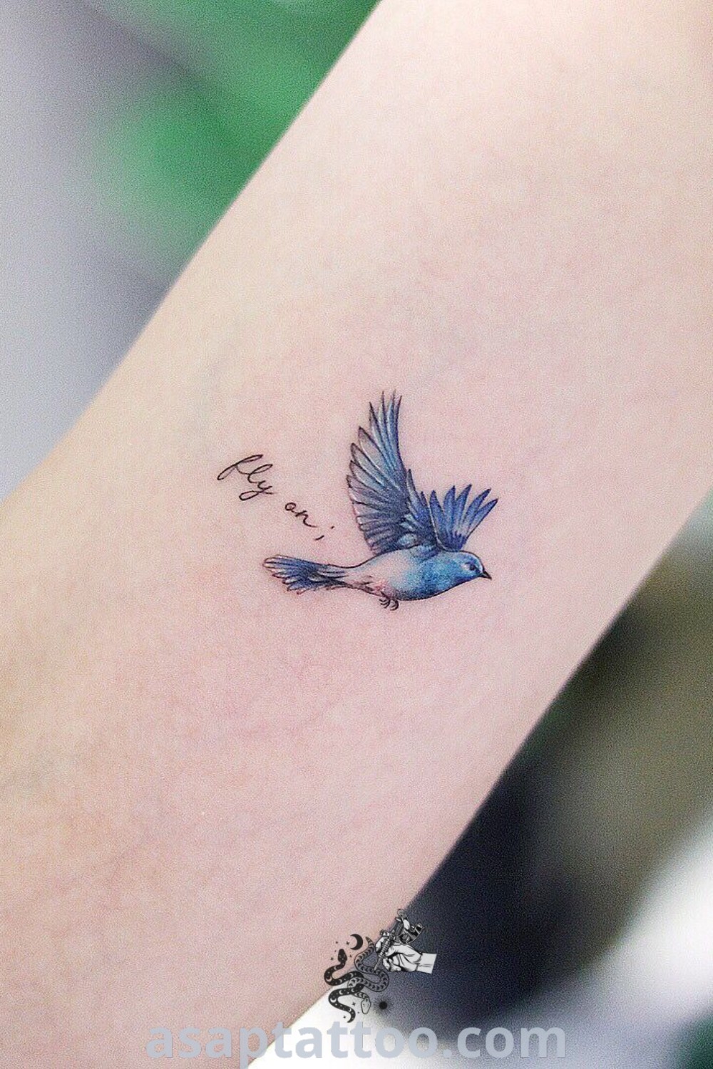 Small blue bird memorial tattoo featuring a blue jay flying away from the word love on a woman