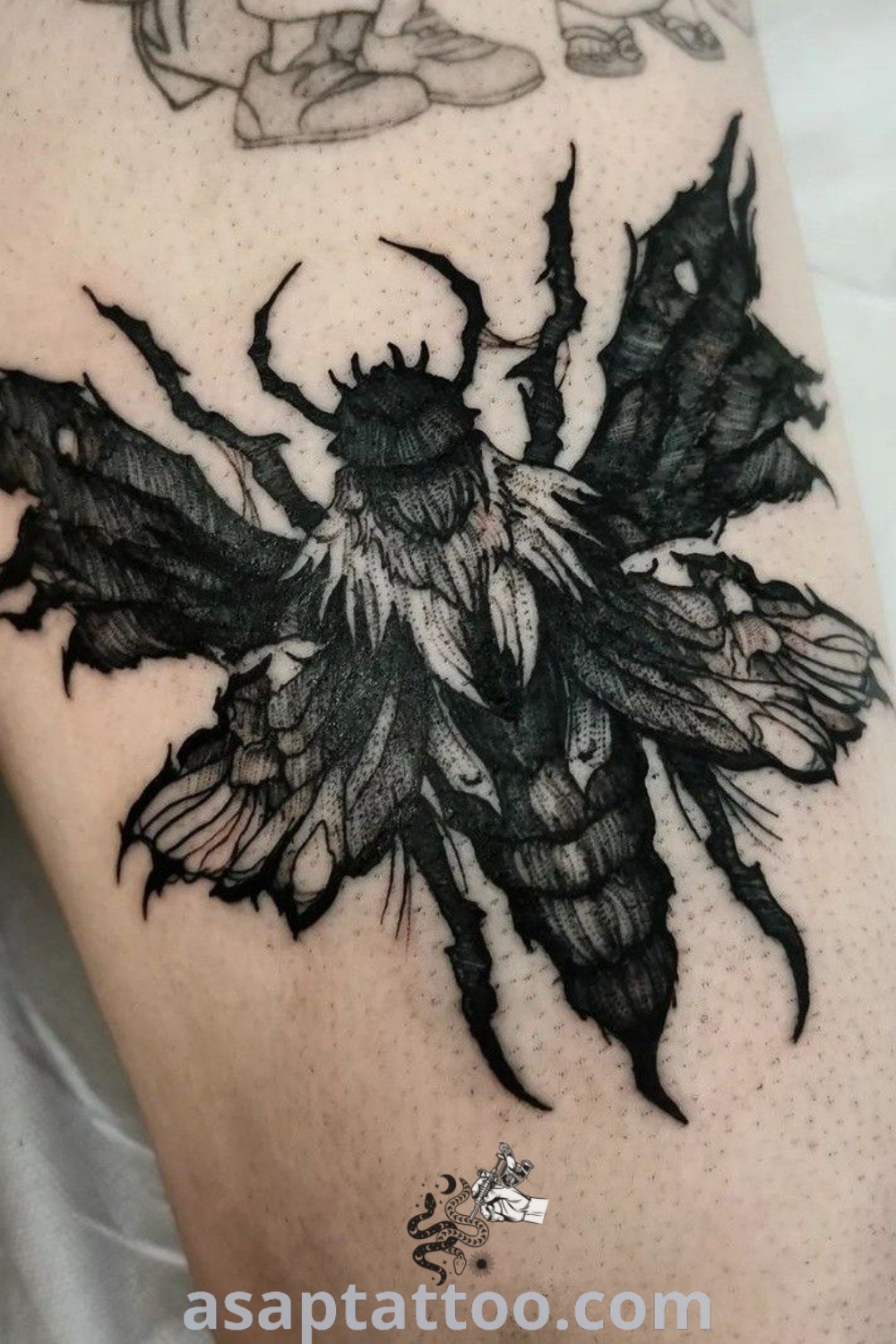 Close-up of a person’s legs showcasing amazing bug tattoos including a gothic bee tattoo and a deathhead moth tattoo in black and grey. Unique body art ideas for men looking for tattoos to inspire them, featured on asaptattoo.com.